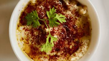 A bowl of creamy dip with a garnish of parsley and a sprinkle of red spice.