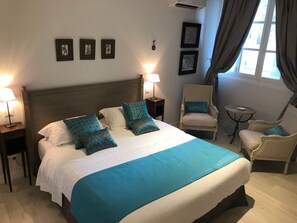Relax in comfort with a large bed, bedside table, and chair, surrounded by framed pictures and natural light.
