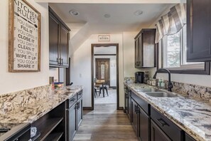 A kitchen with marble countertops, dark cabinets, and a sign listing kitchen rules.