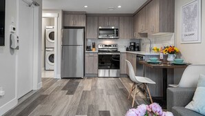 A modern kitchen with stainless steel appliances, a dining area with a white chair, and a wall-mounted map.