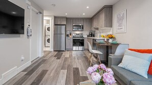 A modern kitchen with stainless steel appliances, a dining area with a table and chairs, and a living room with a sofa and decorative flowers.
