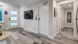 A hallway with a flat-screen TV mounted on the wall, a door with a security camera, and a framed picture on the wall.