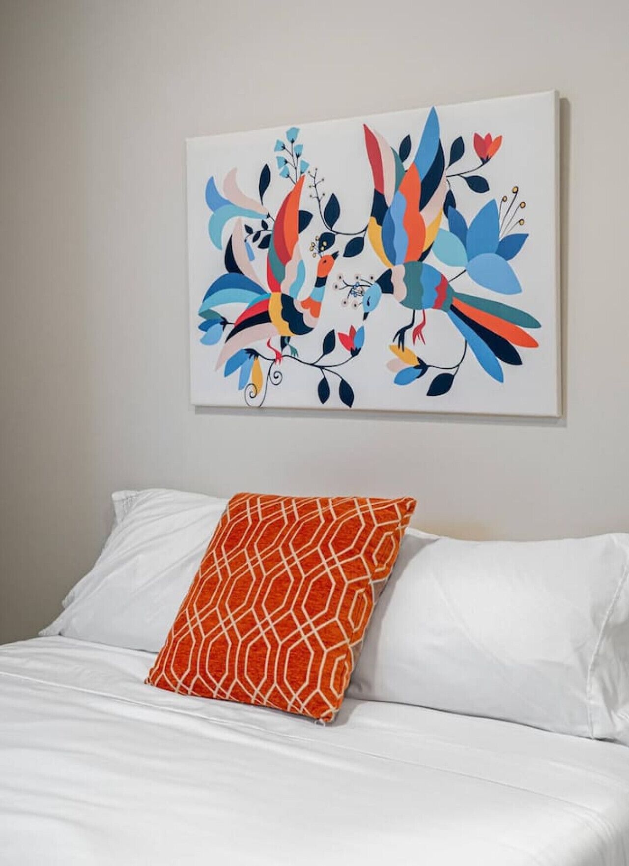 A bed with white linens and a single orange patterned pillow.