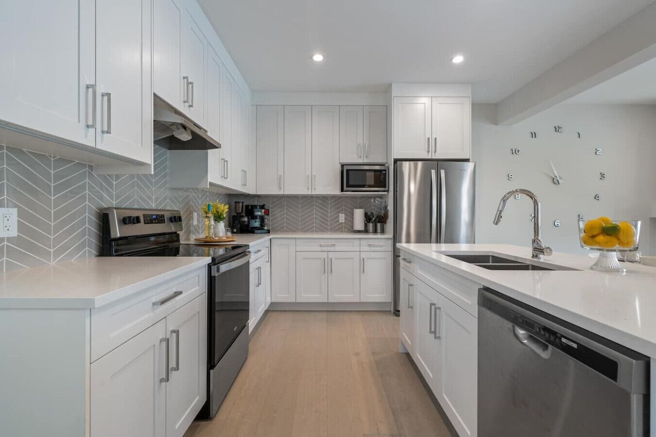A modern kitchen with white cabinetry, stainless steel appliances, and a herringbone tile backsplash.
