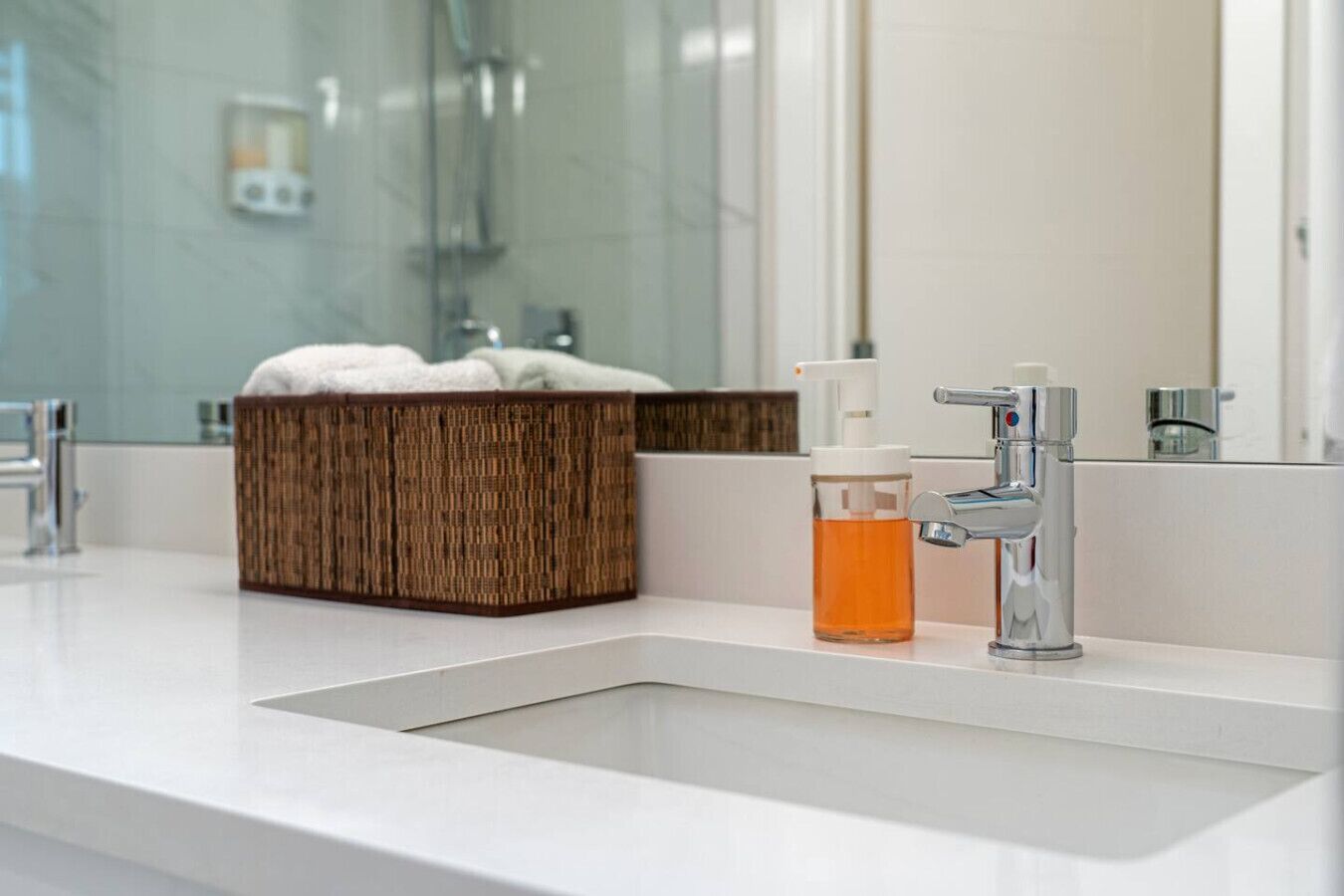 Een moderne badkamer met een witte wastafel, een houten opbergmeubel, een spiegel en een desinfecterende handgeldispenser.