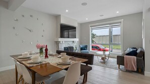 A modern living room with a dining area, a sofa, a TV, and a large window with a view of a red car outside. - Modern 3Br Altadore Home Near Downtown (Calgary)