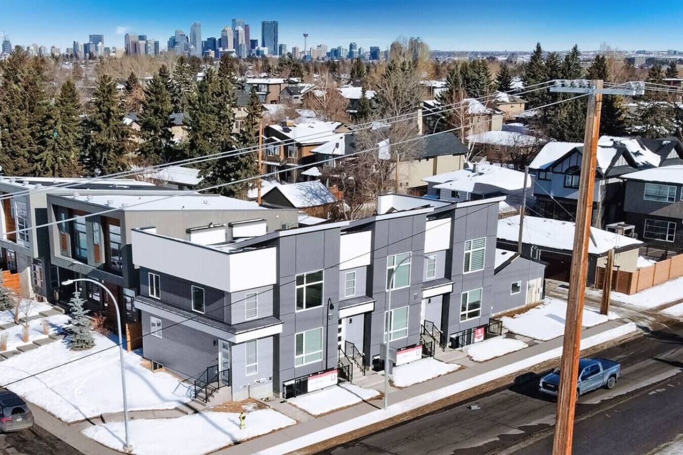 A modern multi-story residential building with a flat roof, visible balconies, and a parking area.