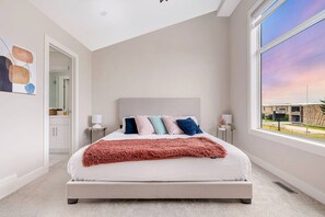 A bedroom with a bed, bedside tables, a window with a view, and a door leading to a bathroom.