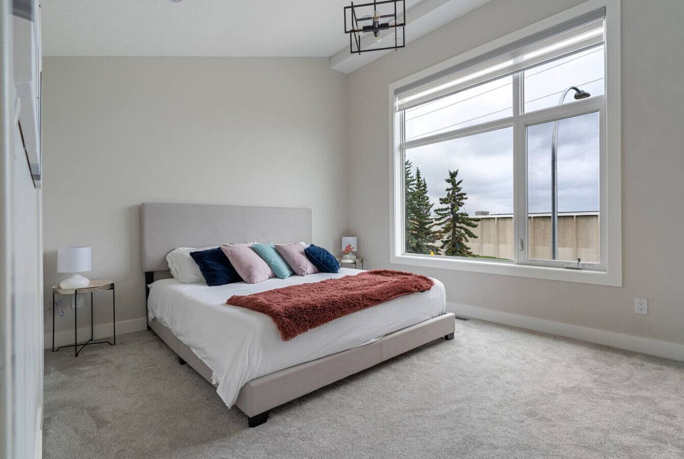 A bedroom with a bed, a nightstand, a lamp, and a large window with a view of trees.