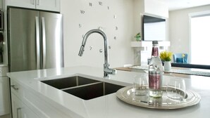 A modern kitchen with a stainless steel refrigerator, a sink with a chrome faucet, and a tray with glasses and a bottle. - Modern 3Br Altadore Home Near Downtown (Calgary)