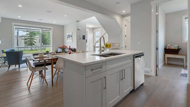 A modern kitchen with a central island, a dining area with a blue chair, and a view of the outdoors. - Modern 3Br Altadore Home Near Downtown (Calgary)