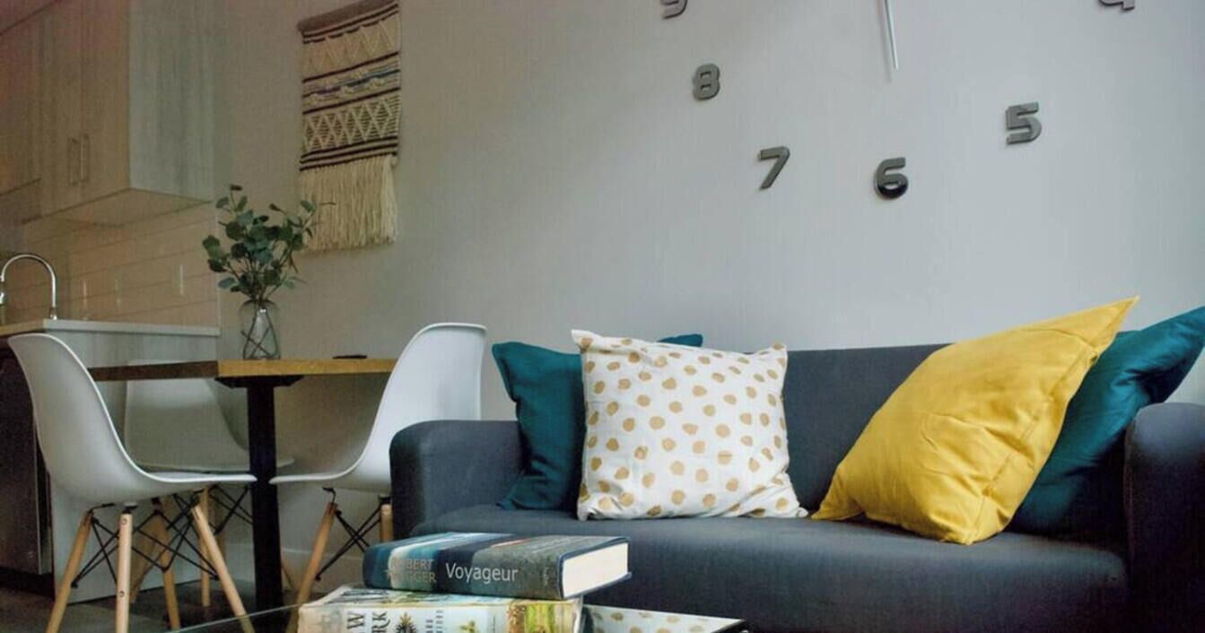 A modern living room with a sofa, a coffee table with books, a dining area with a chair, and a wall with numbers.