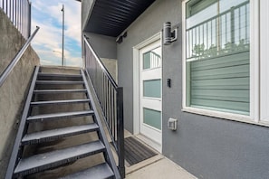 A staircase leading to a door with a window, a wall-mounted light, and a security camera.