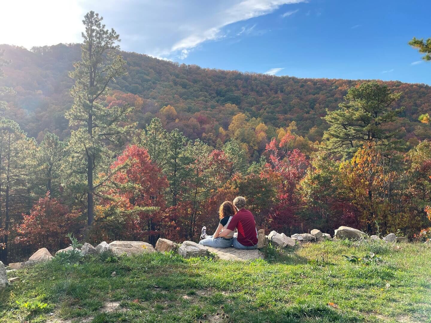 A couple sitting on a rock ledge overlooking a forested hillside.