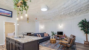 Una cocina moderna con una isla central, armarios de madera oscura y una planta colgante.