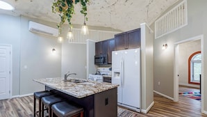 Una cocina con una isla central, suelo de madera y plantas colgantes.