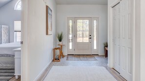 En hall med en vit dörr, ett litet bord med en växt och en matta som leder in till ett sovrum.