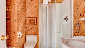 A bathroom with wooden walls, a glass shower enclosure, a toilet, and a sink.