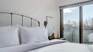 A bedroom with a bed, a nightstand, a wall-mounted lamp, and a sliding glass door leading to an outdoor area. - Bridgehampton Beach Walk (Bridgehampton)