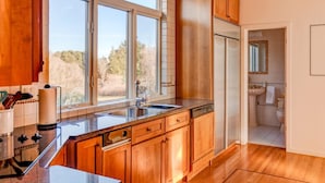 A modern kitchen with wooden cabinets, a stainless steel sink, and a view of the outdoors. - Bridgehampton Beach Walk (Bridgehampton)
