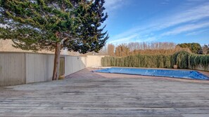 A wooden deck with a blue tarp, a tree, and a hedge.