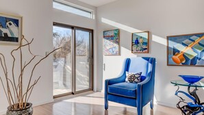 A modern living room with a blue armchair, a glass coffee table, and various artworks on the walls. - Bridgehampton Beach Walk (Bridgehampton)