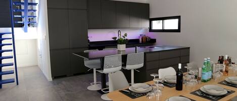 A modern kitchen with dark cabinets, a central island, and a dining area with a wooden table set for six.