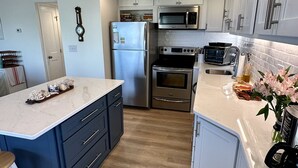 A modern kitchen with a central island, stainless steel appliances, and light wood flooring. - Newly renovated Oceanside condo with easy access to the pool and beach! (Ocean City)