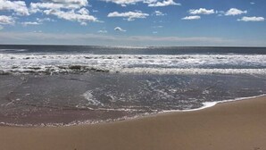 A beach with waves reaching the shore under a clear sky with scattered clouds. - Newly renovated Oceanside condo with easy access to the pool and beach! (Ocean City)