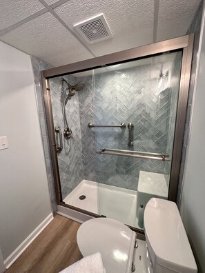 Et moderne badeværelse med et glasafskærmet brusebad, et hvidt toilet og et backsplash af fliser i et fiskebensmønster.
