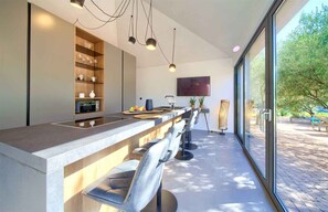 A modern kitchen with a long counter, built-in shelves, a microwave, and a TV mounted on the wall.