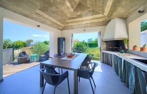 Une terrasse extérieure avec une table à manger, des chaises, un barbecue et une vue sur la verdure environnante.