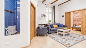 Un salon moderne avec un canapé gris, des poutres en bois au plafond, un radiateur blanc et un mur en briques.