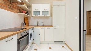 Une cuisine compacte dotée d’un plan de travail en bois, d’un four encastré, d’un lave-linge et de meubles de rangement blancs.