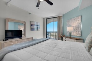 A bedroom with a large bed, a flat-screen TV, a ceiling fan, and a balcony with a view. - Free Beach SRVC! Gorgeous Ocean & Bay Views! Free Beach Bonfires M/F nts (Miramar Beach)