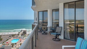 A balcony with a view of the ocean, equipped with chairs and a pool.