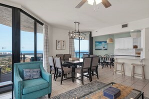 A modern living room with a dining area, large windows with a view of the sea, and a kitchen with white cabinets. - Free Beach SRVC! Gorgeous Ocean & Bay Views! Free Beach Bonfires M/F nts (Miramar Beach)