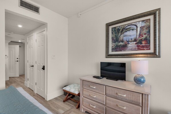 Ein Hotelzimmer mit Bett, Fernseher, Lampe, Kommode und einem Bild an der Wand.