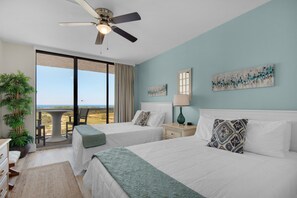 Ein Schlafzimmer mit zwei Betten, einem Deckenventilator, Meerblick und einem großen Fenster.