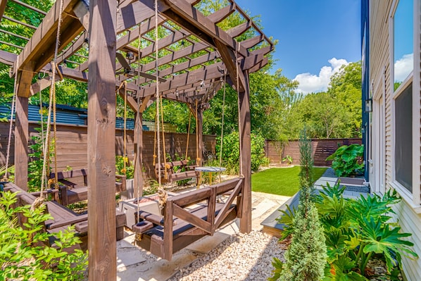Une pergola en bois avec des balançoires et une table, installée dans un coin du jardin.