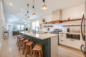 Une cuisine moderne dotée d’un grand îlot central, de tabourets en bois et d’appareils électroménagers intégrés.