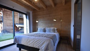A modern bedroom with a large bed, wooden ceiling beams, and a sliding glass door leading to a balcony. - Chalet for 8 people with Terrace / Garden / Spa - 5 rooms - 4 bedrooms (Montriond)