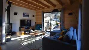 A modern living room with a wooden ceiling, a large TV, a sofa, and a dining area. - Chalet for 8 people with Terrace / Garden / Spa - 5 rooms - 4 bedrooms (Montriond)