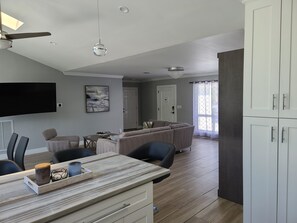 Een moderne woonkamer met een flatscreen televisie, een eethoek met een houten tafel en een keuken met witte keukenkastjes.