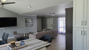 Ein modernes Wohnzimmer mit einer Sofagarnitur, einem Essbereich mit einem Marmortisch und einer Küche mit weißen Schränken.