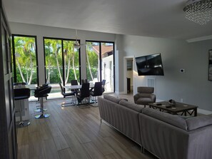 Een moderne woonkamer met een grote bank, een aan de muur bevestigde televisie en een eethoek met een tafel en stoelen.