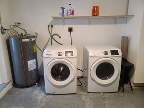 A laundry area with two washing machines, a water heater, and a shelf with cleaning supplies. - Private Newly Renovated Home - Short Walk to Beach, Food, Shopping & More!!! (Lauderdale-by-the-Sea)