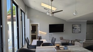 Eine moderne Küche mit einer großen Kochinsel, schwarzen Stühlen, einem Flachbildfernseher und einem Deckenventilator.