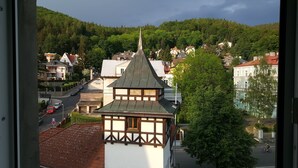 Ein traditionelles Gebäude im europäischen Stil mit einem steilen Dach und einem Spitzenturm, umgeben von üppiger Vegetation und Wohnhäusern.