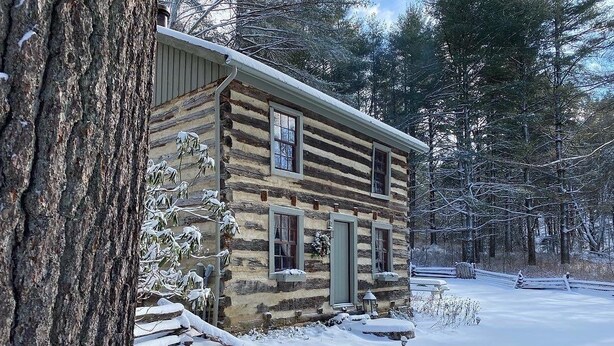 A log cabin with a snow-covered exterior, surrounded by trees.